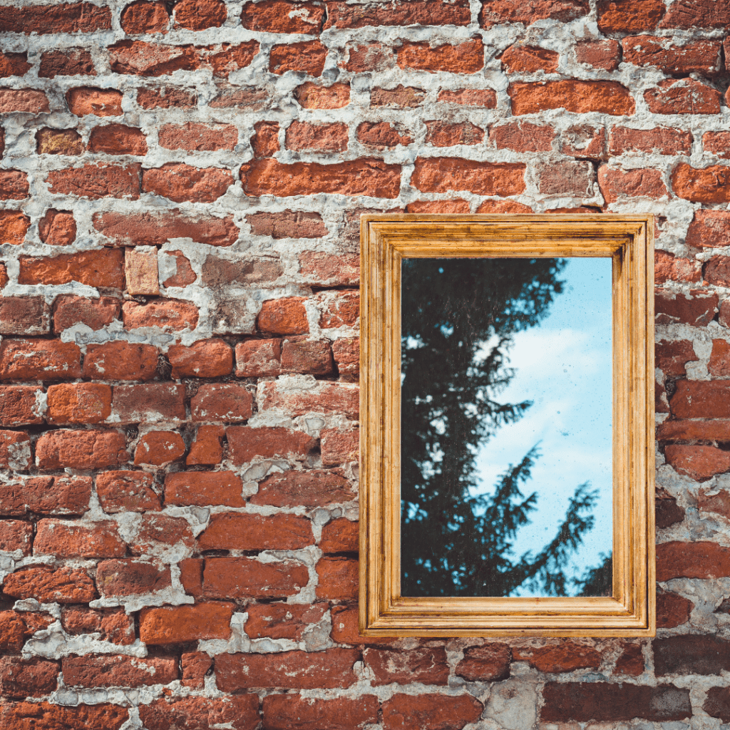 brick wall with a hanging gold mirror that is reflecting green tree